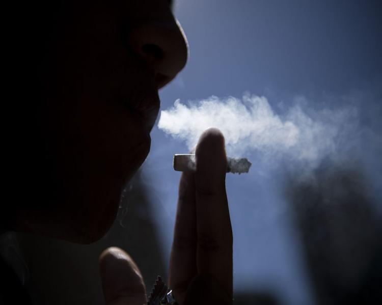 Rosto de perfil e mão segurando cigarro próximo à boca, que solta fumaça