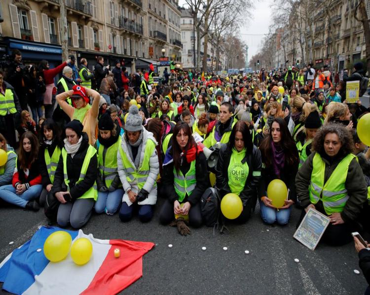 Pessoas agachadas, usando coletes amarelos em manifestação na rua, em Paris