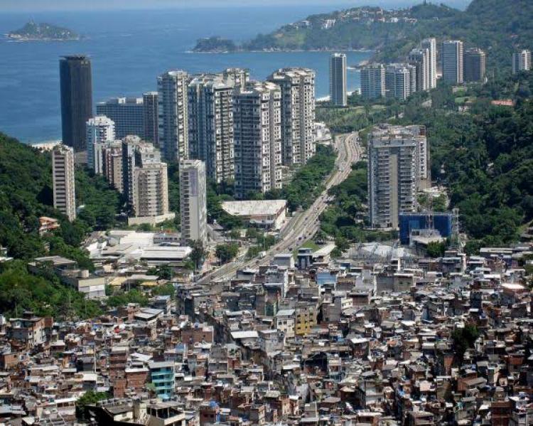 Favela em primeiro plano e prédios altos próximos ao mar, ao fundo