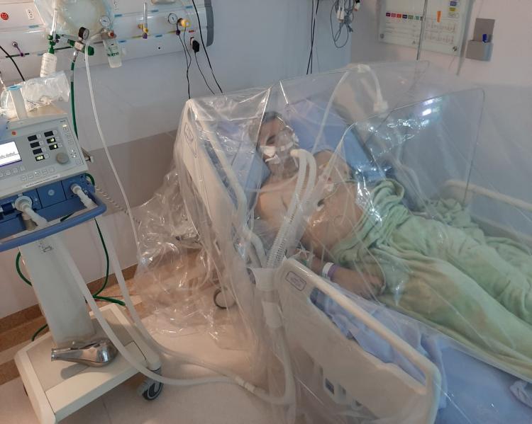 Quarto hospitalar, com equipamentos e cama hospitalar na qual um boneco, simulando um homem está deitado, sobre uma proteção plástica