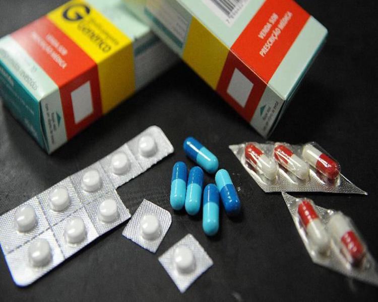 Caixas e cartelas de medicamentos espalhadas e alguns comprimidos soltos