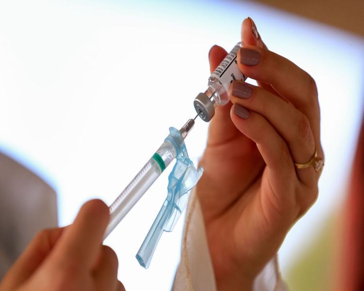 Mãos seguram uma seringa inserida em um frasco de vacina