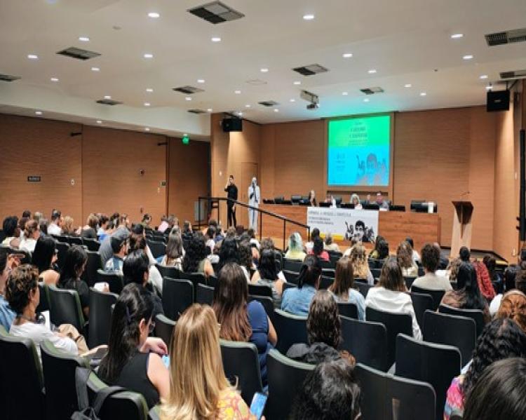 Plateia assiste a apresentação de integrantes de uma mesa de debates ao fundo