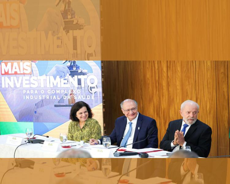 Uma mulher e dois homens de terno estão em uma mesa de evento e sorriem