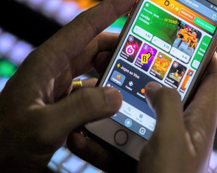 Mãos mexem na tela de um celular, que mostra ícones de sites de apostas